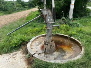 a community borehole or handpump in a rural East African setting, with water being drawn