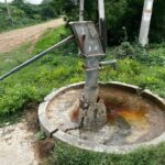 a community borehole or handpump in a rural East African setting, with water being drawn